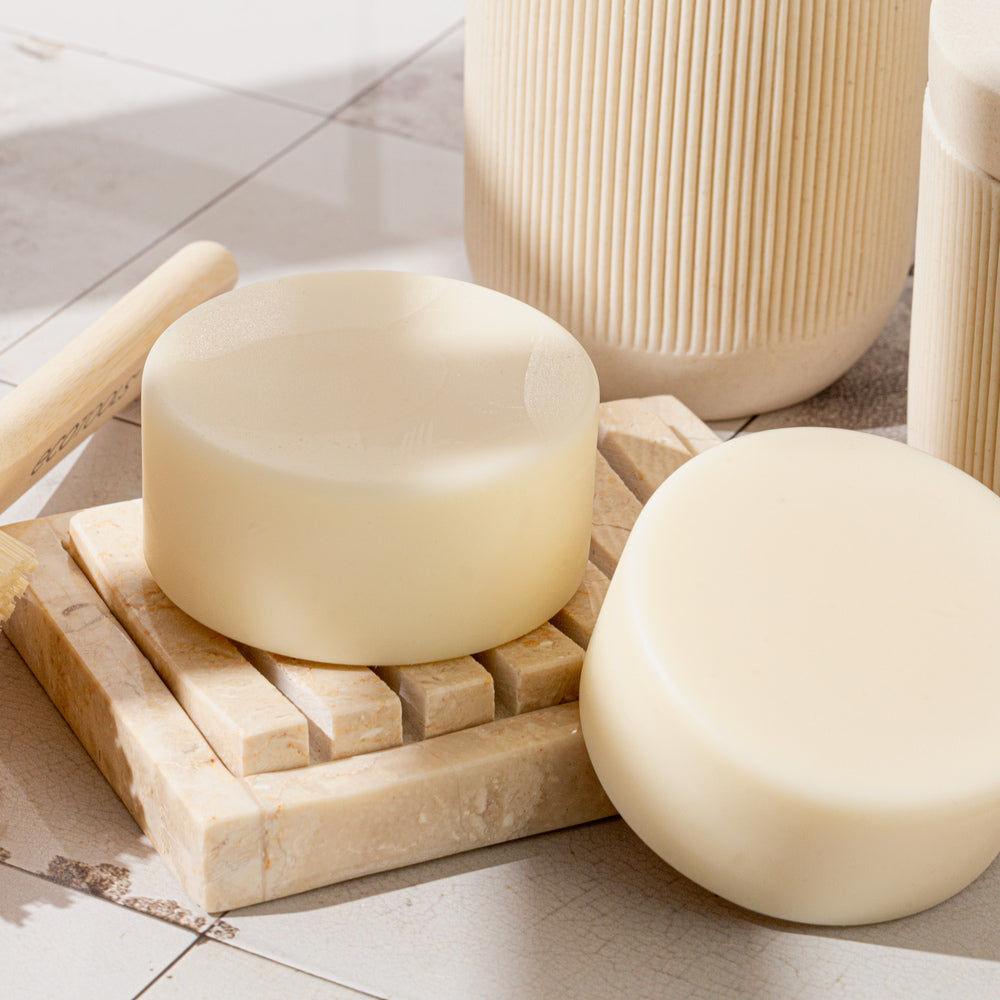 Round conditioner bars on marble soap dish with wooden brush and neutral bathroom accessories nearby