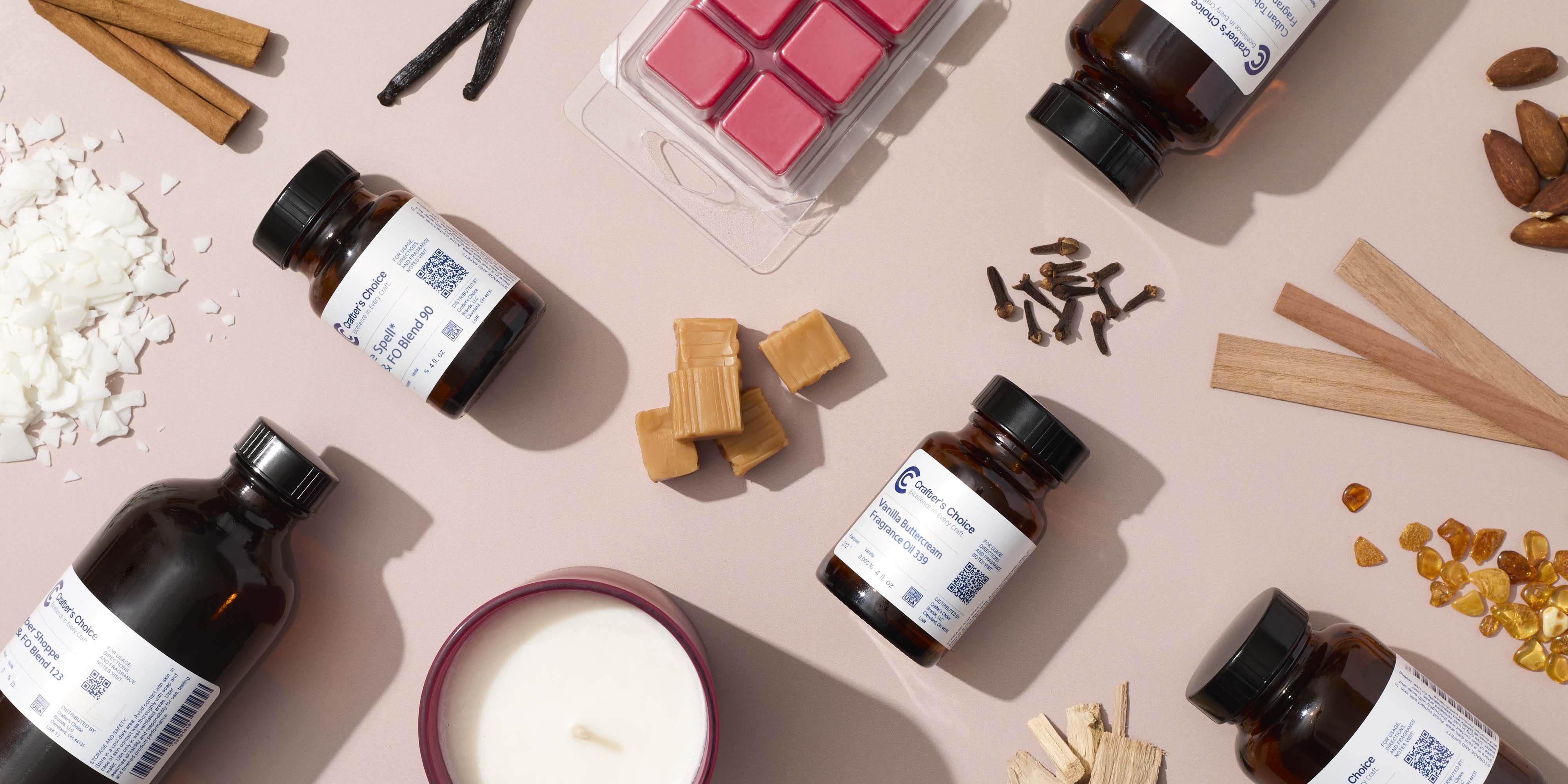 Flat lay of candle making supplies on a soft pink background, featuring fragrance oil bottles, wax flakes, wax melts, a finished candle, and warm scent ingredients like cinnamon sticks, vanilla beans, cloves, woods, and amber pieces.