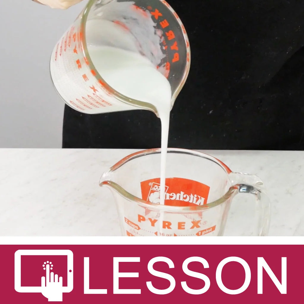 White soap in a clear glass measuring cup being poured into another clear glass measuring cup