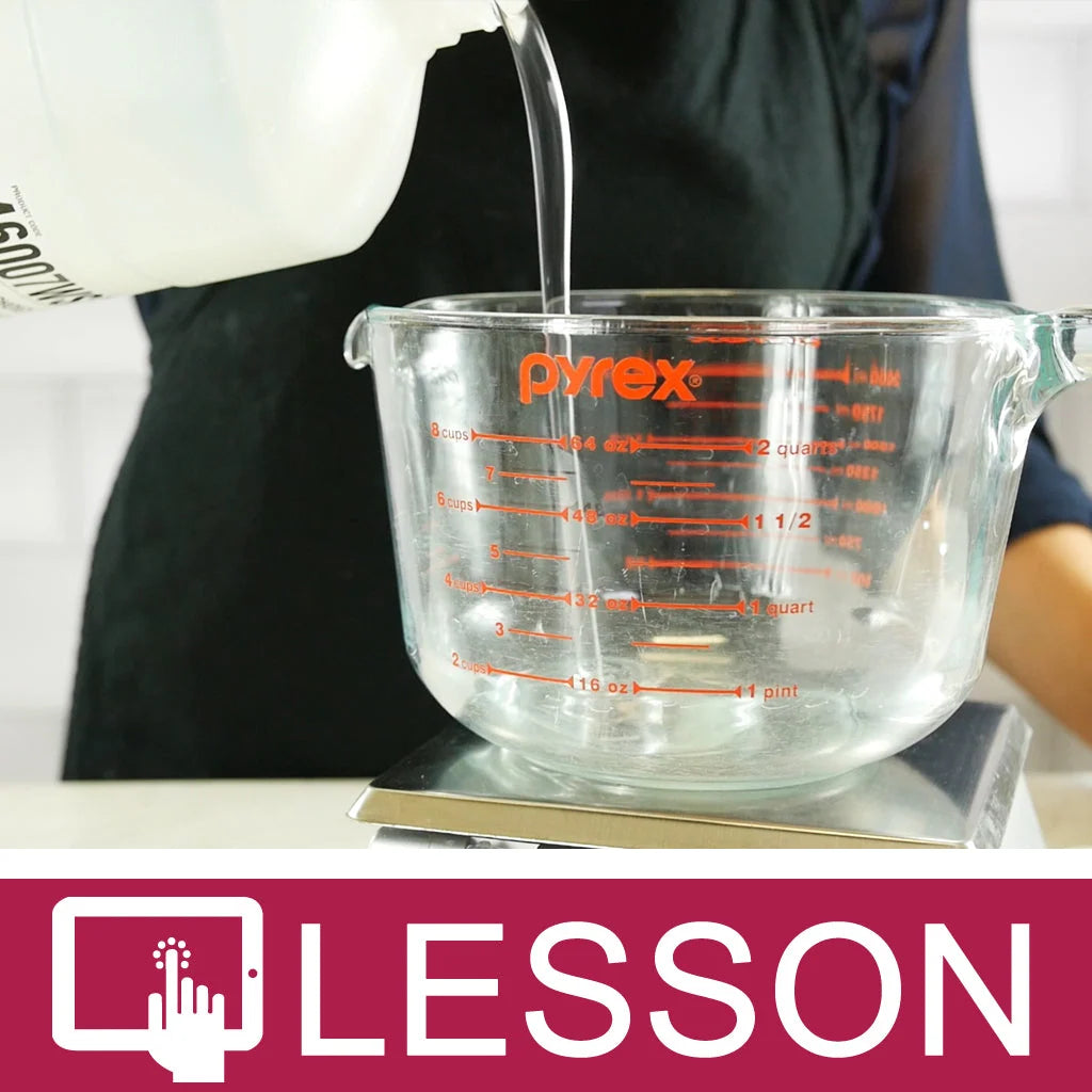 Someone pouring clear soap into a clear pyrex measuring glass cup on a scale