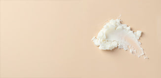 Close-up of a thick, creamy white skincare butter spread across a soft beige background, highlighting its rich texture.