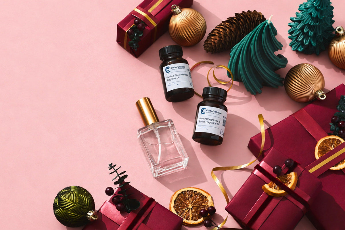 Holiday fragrance-making scene with perfume bottle and fragrance oils surrounded by red gifts, gold ornaments, green tree candles, pinecones, dried oranges, and ribbon on a pink background.