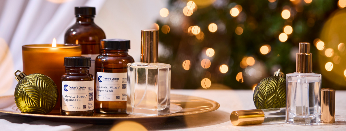 Crafter’s Choice Lafayette Street and Greenwich Village fragrance oils displayed on a gold tray with a lit candle, perfume bottle, and gold ornament. A second perfume bottle sits nearby against a softly glowing Christmas tree.