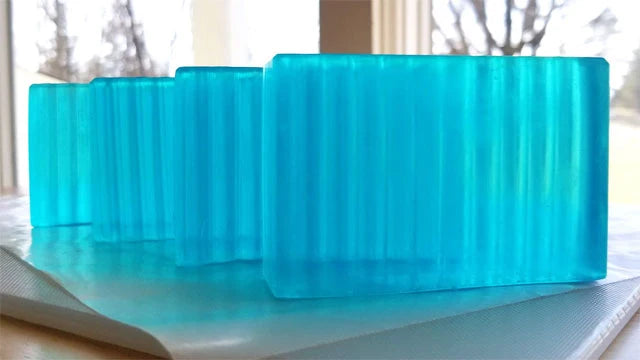 4 translucent blue soaps on a countertop with windows and trees in the background