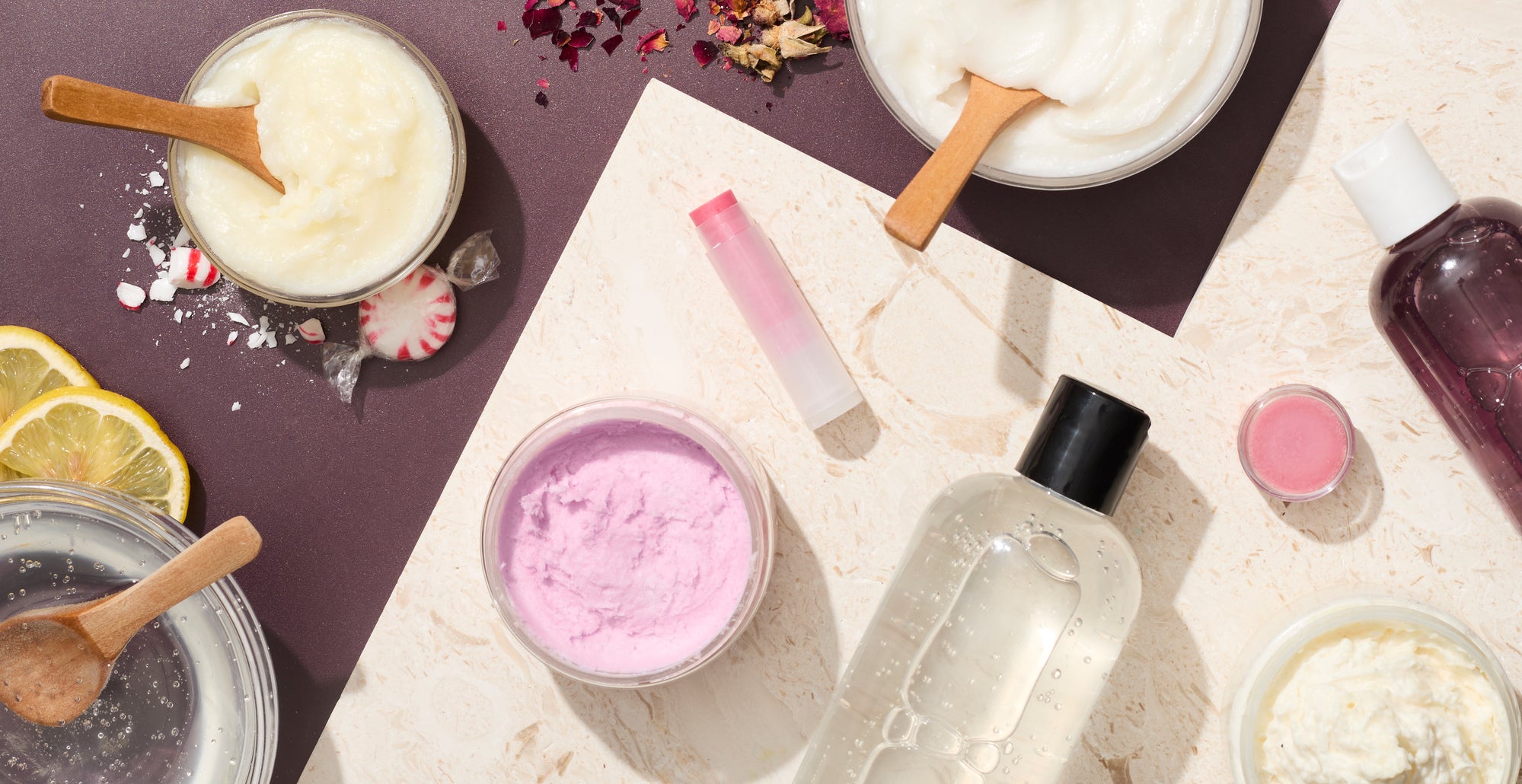 Flat lay of handmade beauty and personal care products on a neutral background, including jars of creams and scrubs, lip balm, bottles, wooden spoons, dried botanicals, lemon slices, and pastel textures arranged in a clean, modern layout.
