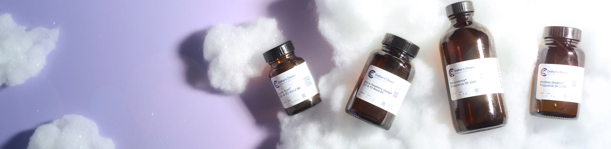 Four amber glass fragrance oil bottles labeled Crafters Choice—Love Spell, Black Raspberry Vanilla, Moondance, and Endless Dreams—rest on fluffy cotton clouds against a soft purple-to-white gradient background.