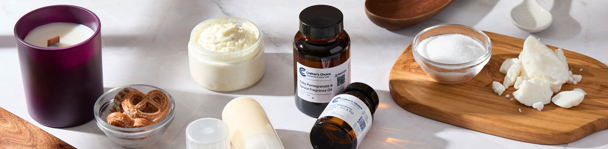 Crafter’s Choice fragrance oils, a purple jar candle, whipped body butter, and bath and body ingredients arranged on a marble surface.