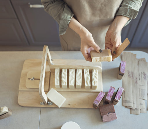 Person using a wooden block cutting tool cutting soap on a light-colored surface